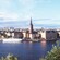 A boat harbor fronts a crowded city with a few church spires protruding above the rest of the buildings
